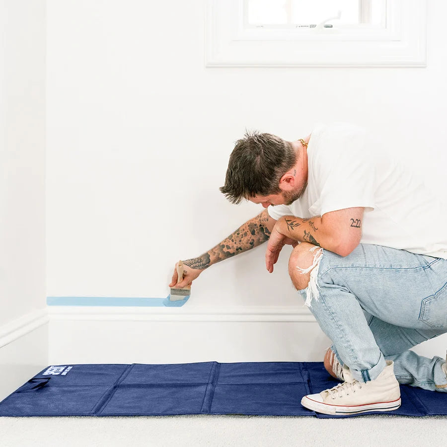 A painter is sitting on a Zibra Speed Drop cloth to tape up a wall