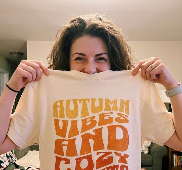 A crafter holds up a tee printed with Autumn Vibes and Cozy Nights