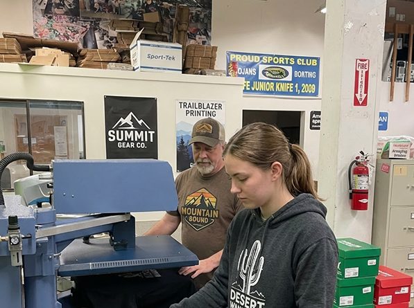 Two people work a heat press in a print shop