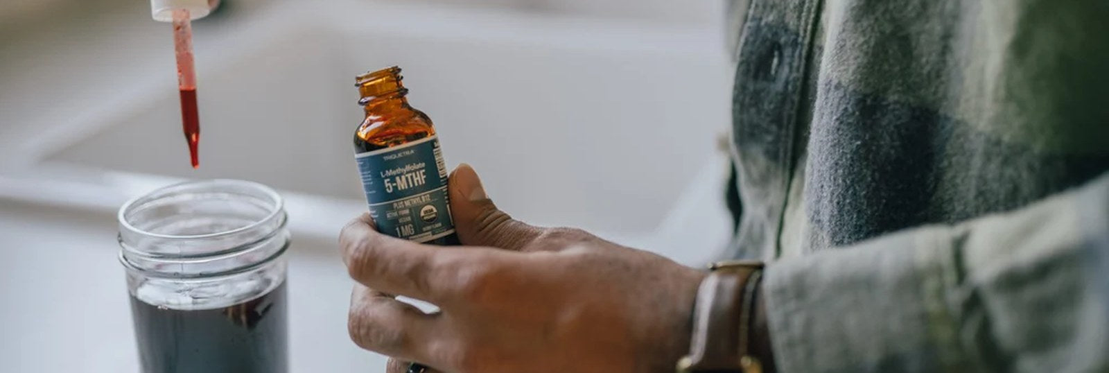 A hand presents a Triquetra liquid supplement bottle next to a dropper and a glass filled with water.