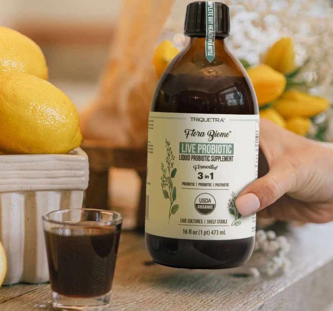 The Triquetra live probiotic tonic bottle is seen with lemons and a glass that has been poured