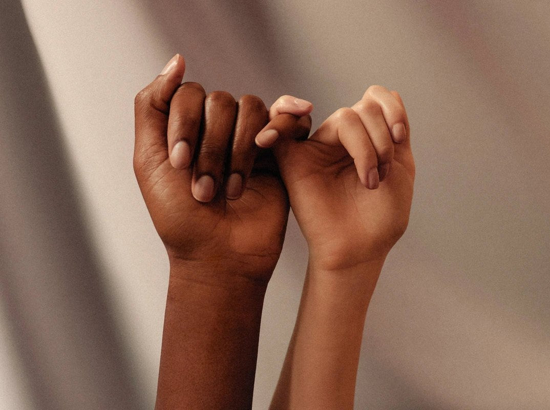 Two hands link little fingers against a soft grey backdrop