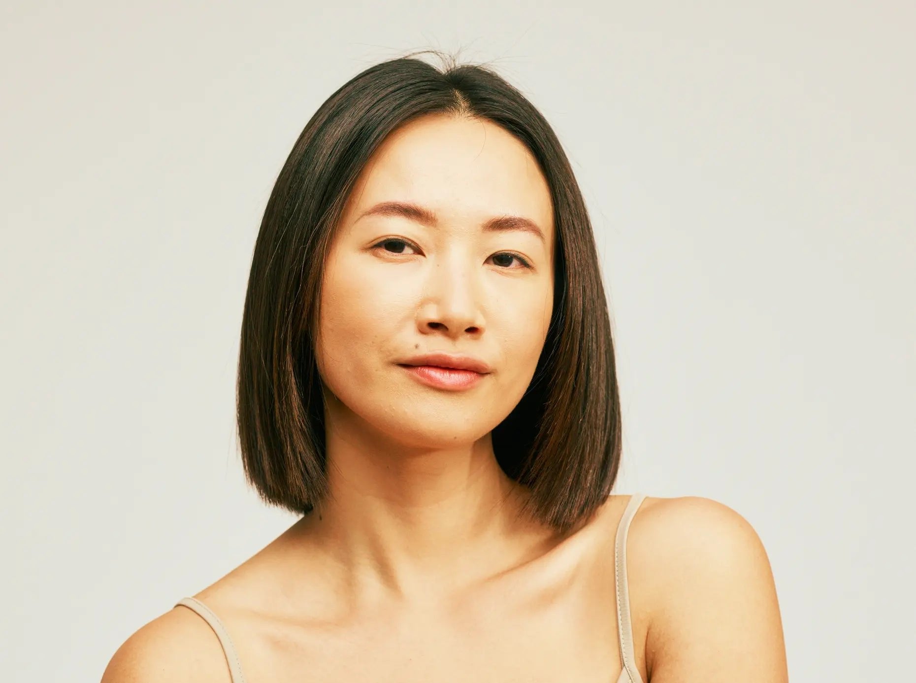 A woman with a dark bob looks into the camera against a pale background