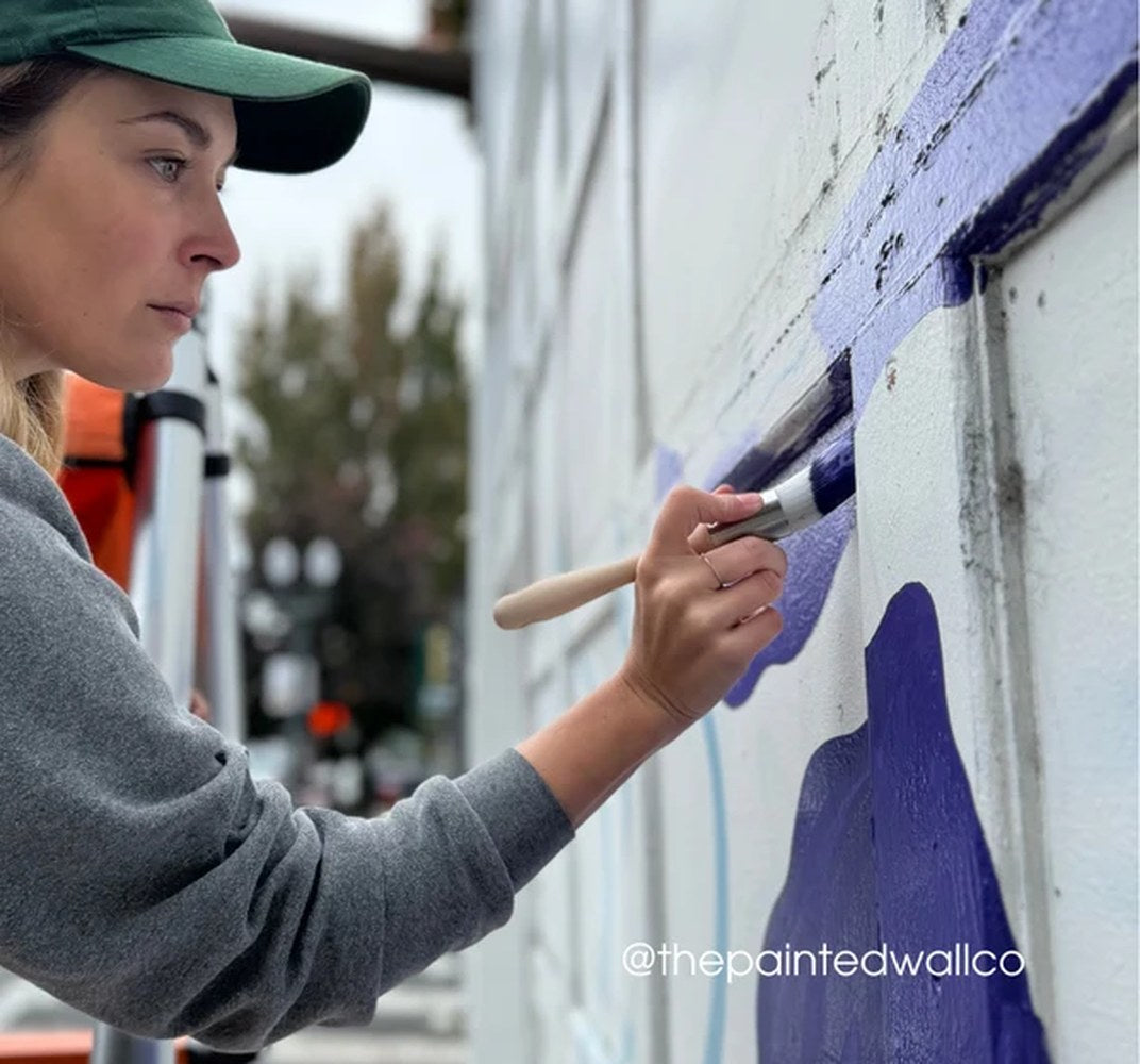 The muralist is painting a blue mural on a wall, using the Zibra brush