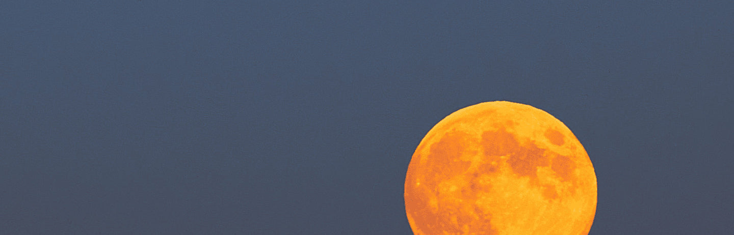 An orange moon in a pale blue sky
